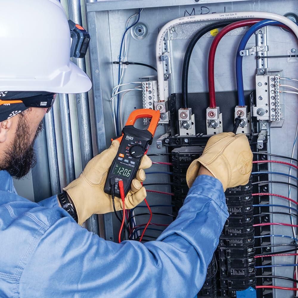 Person wearing safety gear using Klein Tools clamp meter to measure voltage in a circuit breaker panel; display reads 240.5 volts.