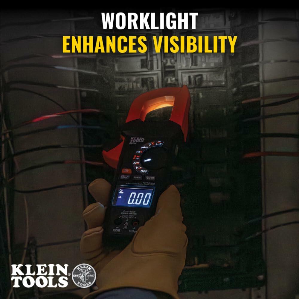 Klein Tools clamp meter in use with built-in worklight illuminating a circuit panel; display reads 0.00 amps, indicating no current detected.