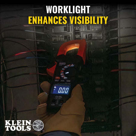 Klein Tools clamp meter in use with built-in worklight illuminating a circuit panel; display reads 0.00 amps, indicating no current detected.
