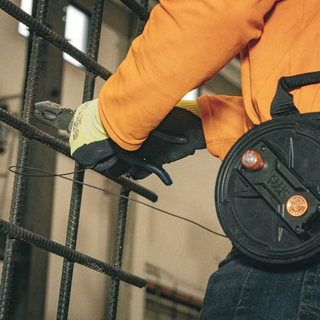 A worker, wearing the tie wire reel on their waist, uses pliers to secure tie wire around vertical rebar. The wire is dispensed smoothly from the reel.
