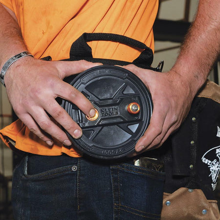 Close-up of a worker wearing the Klein Tools Tie Wire Reel on their belt, ready for use. The image focuses on the quick-lock lid and the rewind knob.