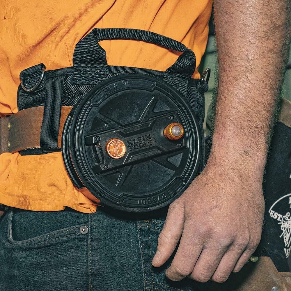 Close-up view of a worker's hand near the Klein Tools Tie Wire Reel on their hip, focusing on the rewind knob and the durable black finish.