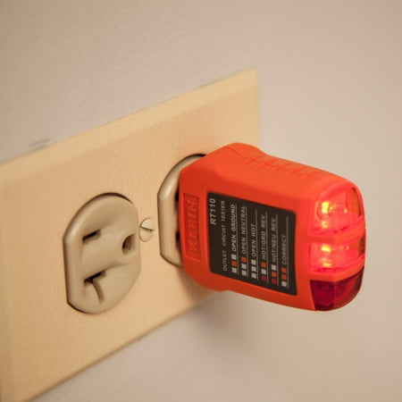 An action shot of the RT110 receptacle tester plugged into a standard residential wall outlet. Two orange LEDs are brightly illuminated, providing a simultaneous visual confirmation of a correctly wired electrical circuit in a home environment.