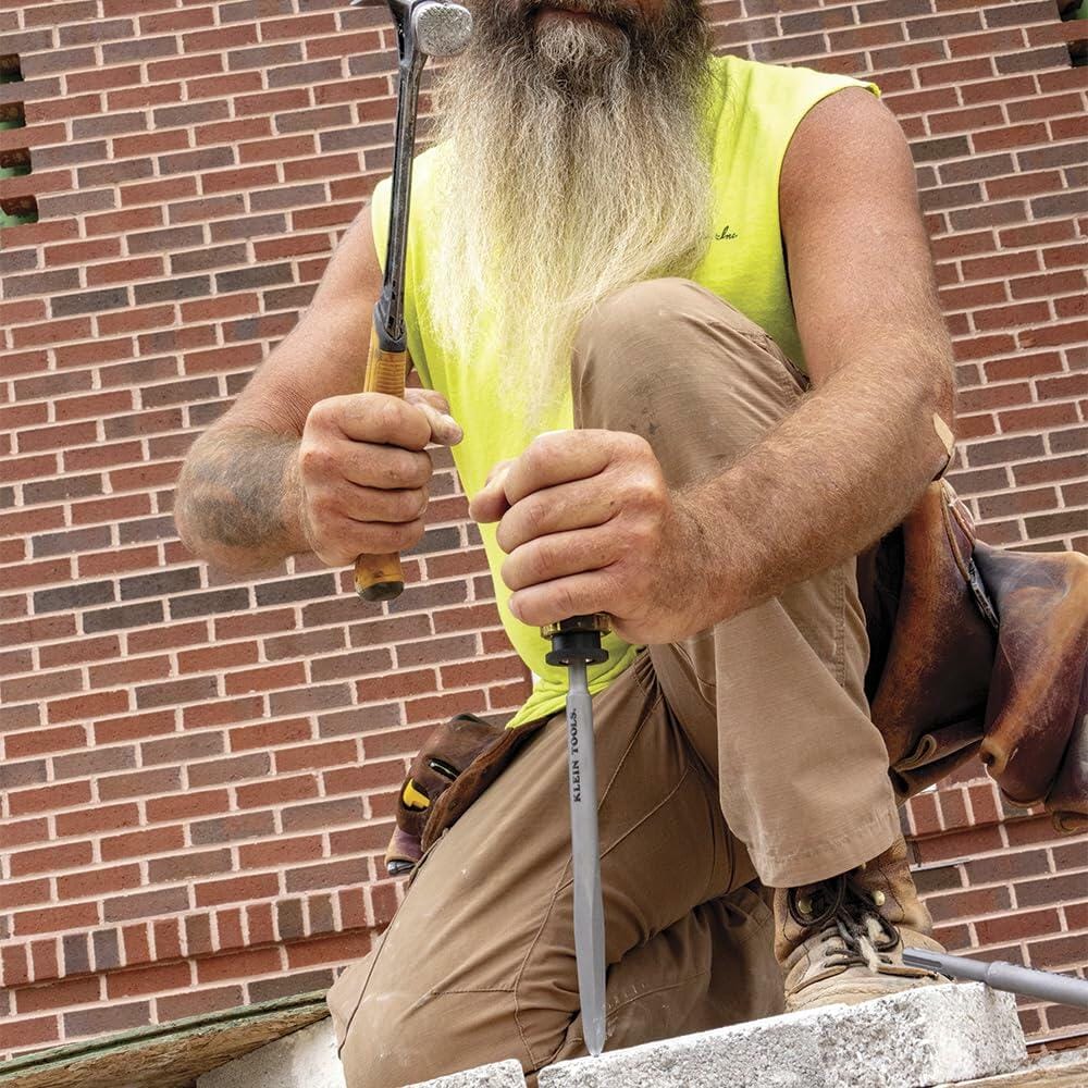 Close-up of construction worker’s hands using hammer and screwdriver to adjust wooden form on concrete surface at outdoor site, with residential building in background.