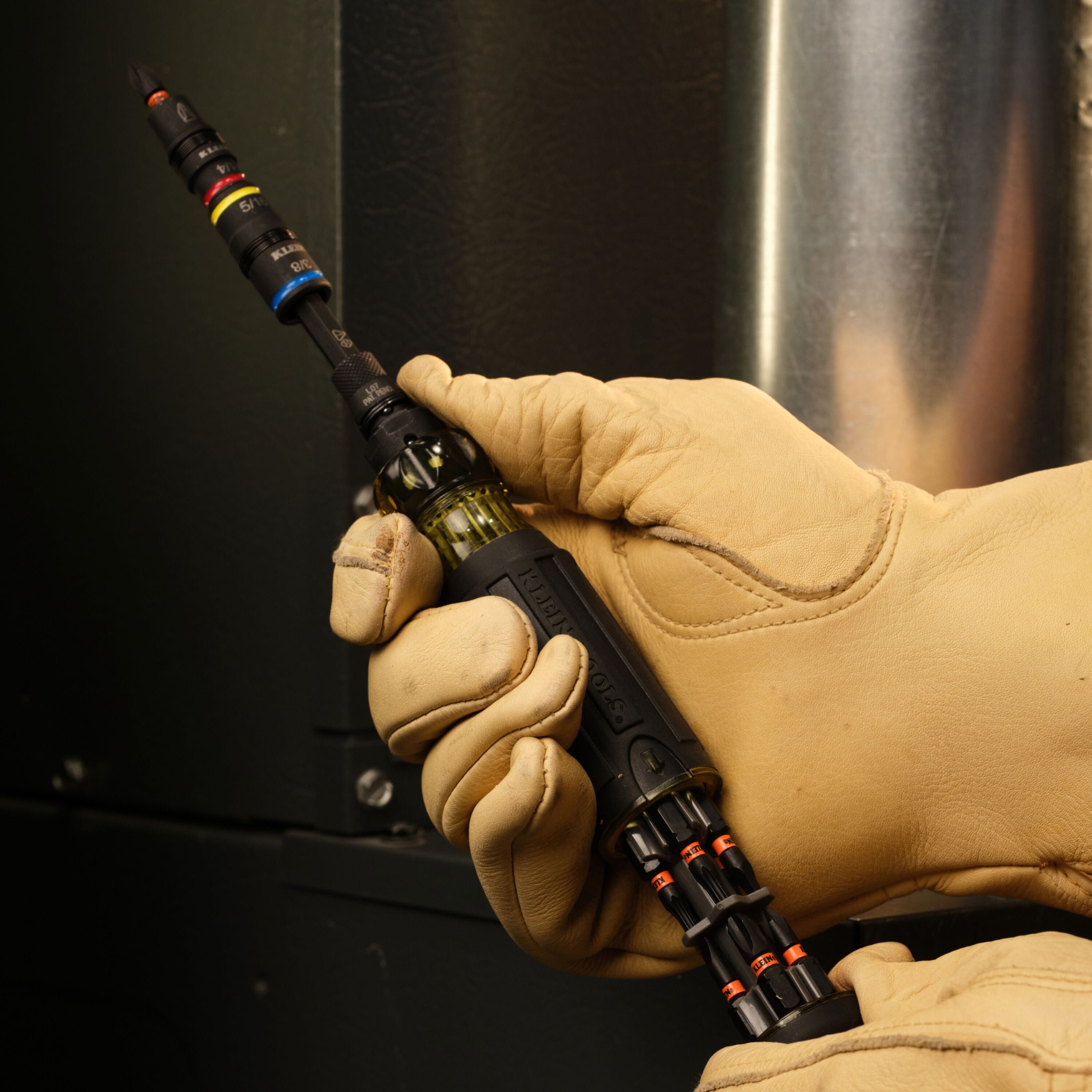 Gloved worker pulling back the onboard bit storage slider on the Klein 32517HD Cushion-Grip screwdriver handle.