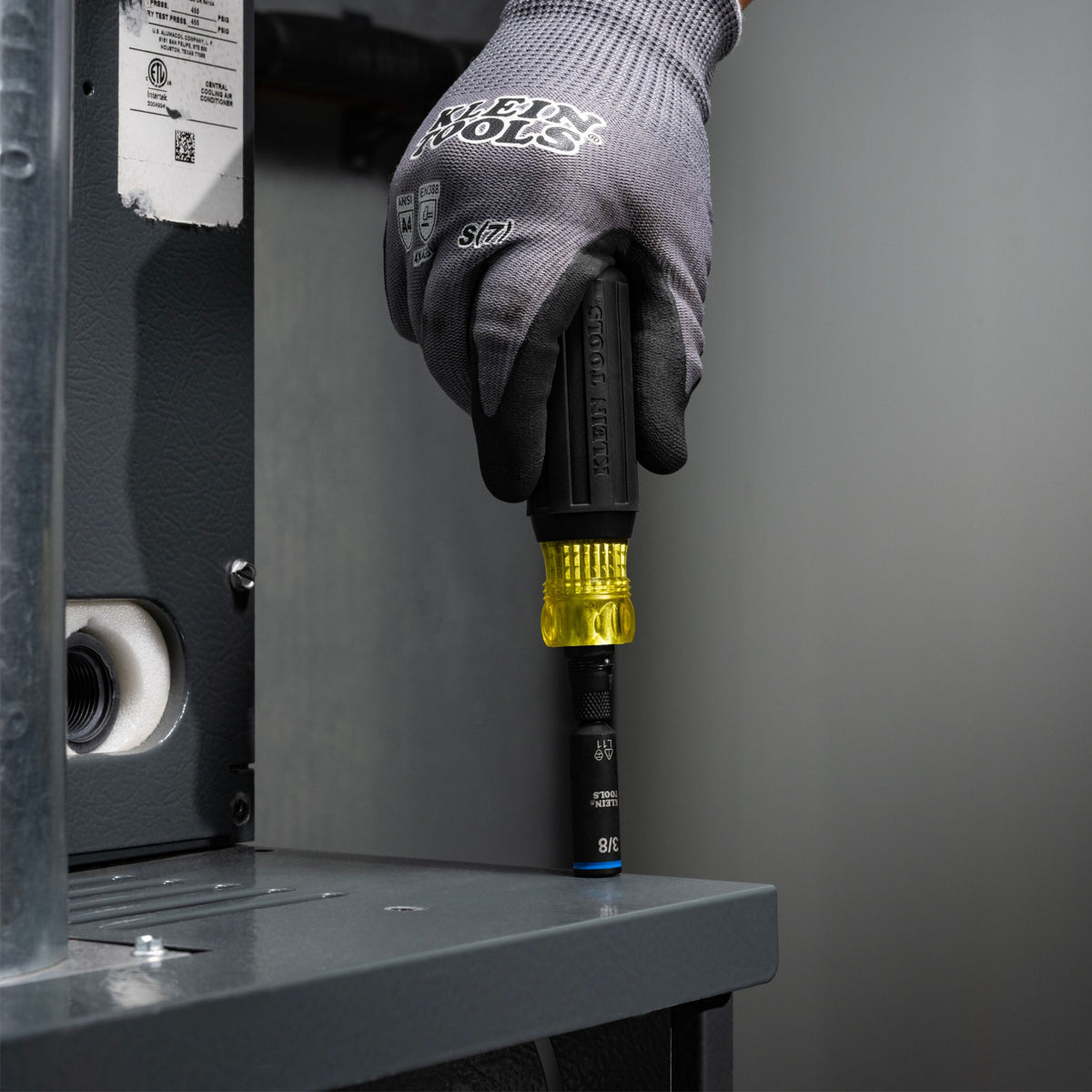 Technician using the Klein 32527HD screwdriver to drive a 3/8-inch hex head fastener on a commercial HVAC unit cabinet top.