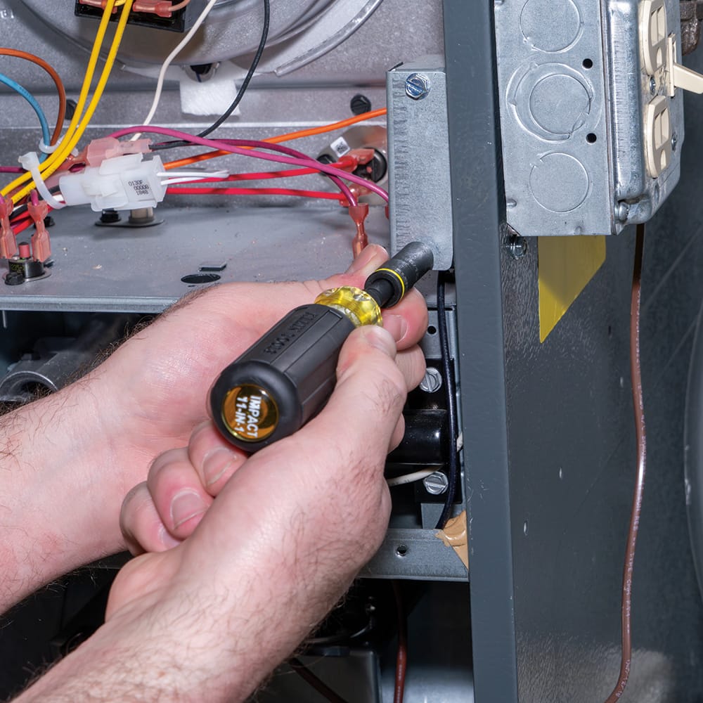 Technician using the Klein Cushion-Grip screwdriver with a 5/16-inch nut driver to fasten a grounded steel box inside an HVAC unit.