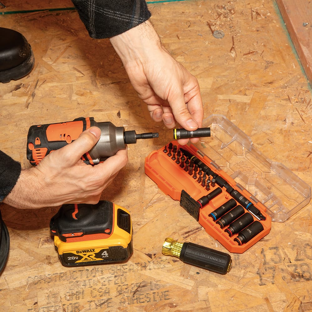 Contractor attaching a 5/16-inch impact socket onto a 1/4-inch quick-connect power adapter next to an open Klein 32502HD storage case.