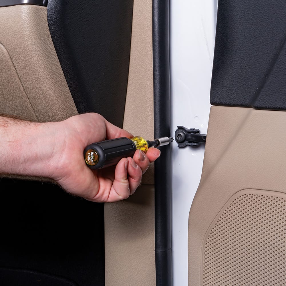 Mechanic using the Klein multi-bit screwdriver to adjust a door hinge fastener in a cramped vehicle door jam clearance area.