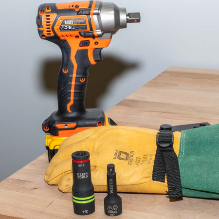 Klein 66044 3-in-1 flip socket and square drive adapter sitting on a workbench next to a 1/2-inch impact wrench and gloves.