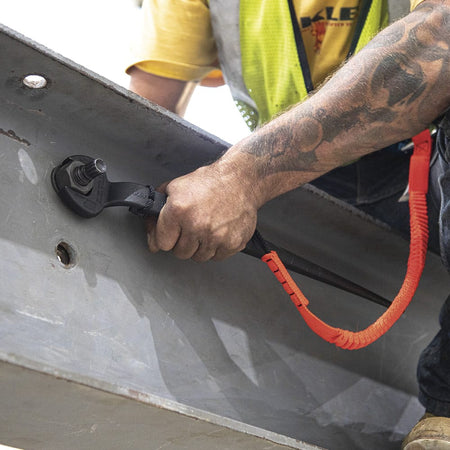 Ironworker using the Klein 3212TT spud wrench attached to an orange fall-protection lanyard to torque a 3/4-inch bolt on a structural steel I-beam.