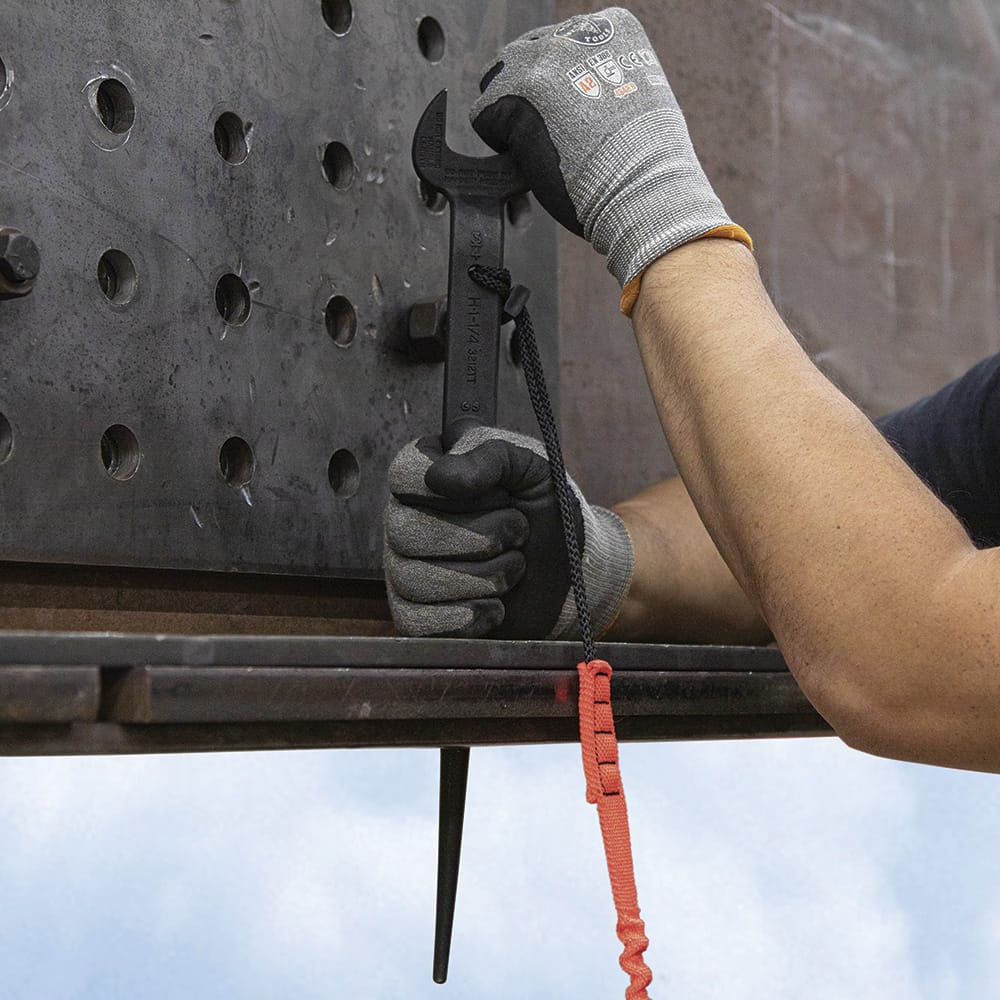 Contractor holding a tethered Klein 3212TT spud wrench vertically while aligning bolt holes on a multi-layer structural steel plate assembly.