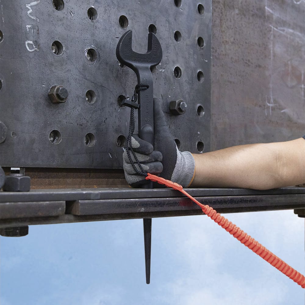 Ironworker holding the tethered Klein 3214TT offset spud wrench next to a heavy structural steel beam joint at an elevated work site.