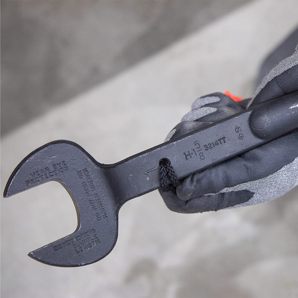 Gloved hand holding the Klein 3214TT spud wrench showing a safety lanyard cord secured through the smooth integrated tether hole.