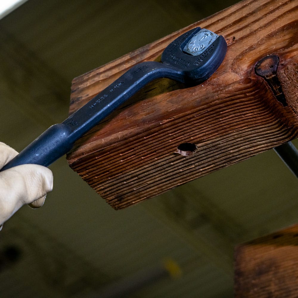 Klein 3222 offset spud wrench engaged on a bolt head demonstrating knuckle clearance along structural wood beam surfaces.