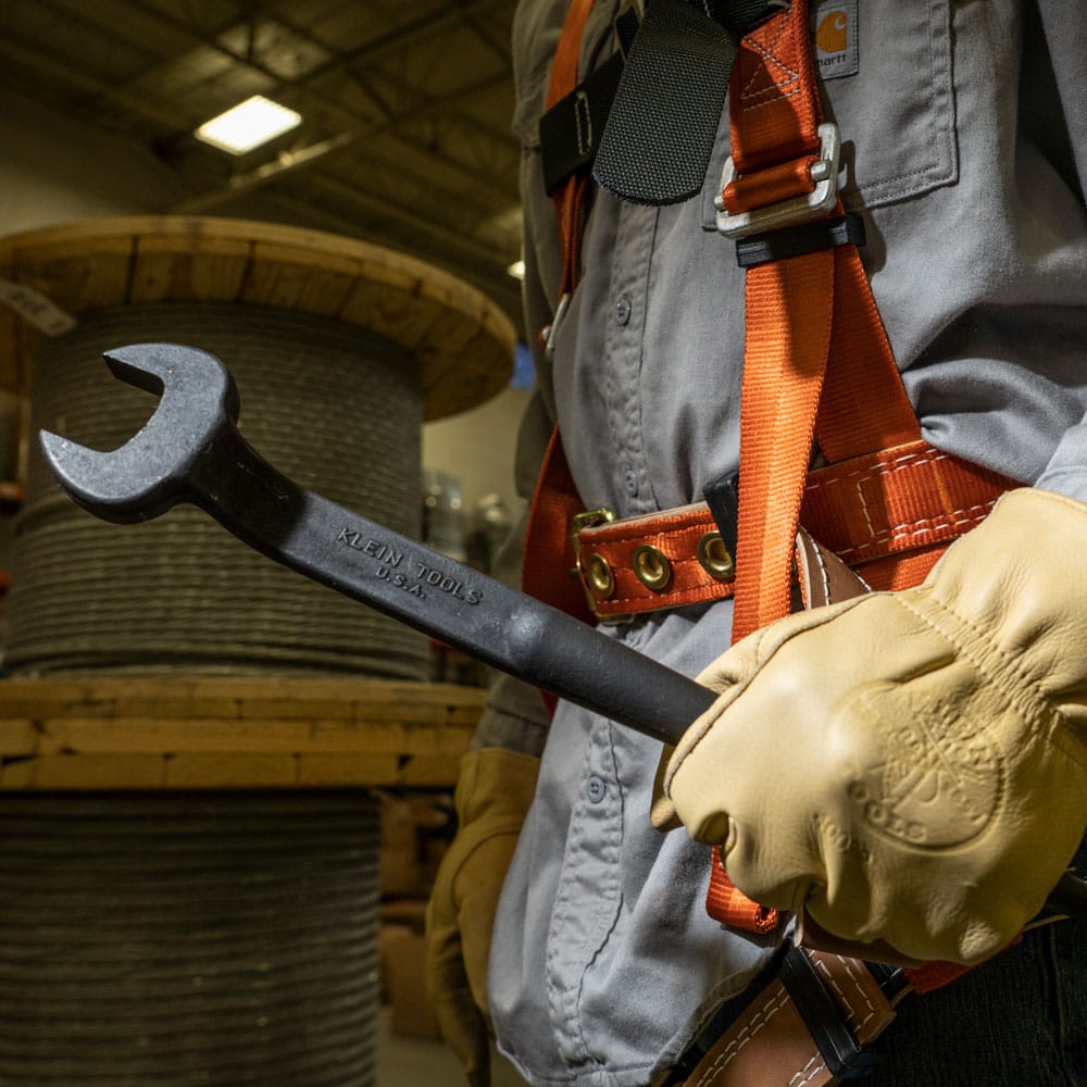 Gloved ironworker holding the Klein 3222 spud wrench displaying the forged alloy steel head and black oxide surface finish.