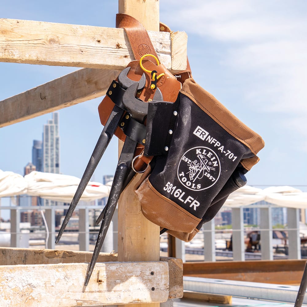 Klein 5860 leather spud wrench holder and canvas bolt bag hanging on wooden jobsite framing while holding two heavy structural connecting wrenches.
