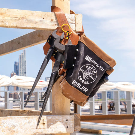 Klein 5860 leather spud wrench holder and canvas bolt bag hanging on wooden jobsite framing while holding two heavy structural connecting wrenches.