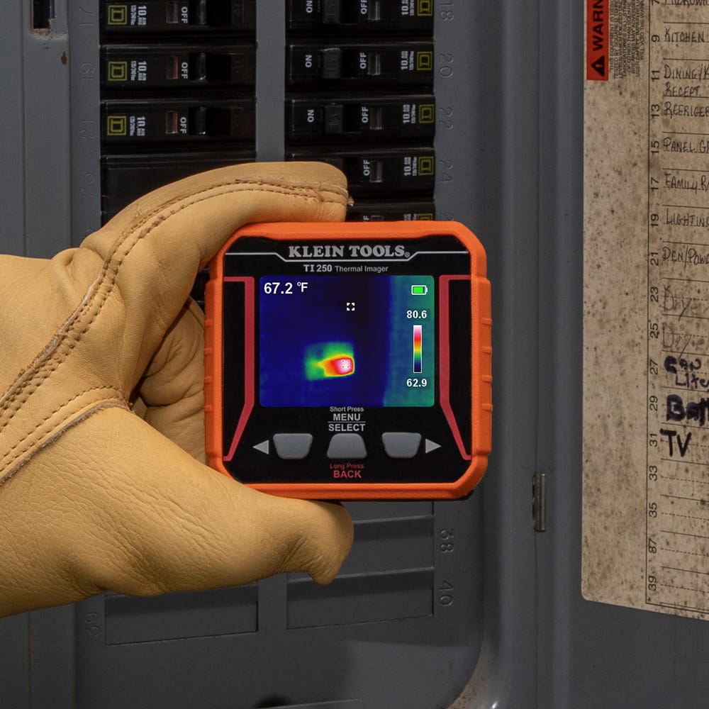 Action shot of a technician wearing protective gloves using the TI250 thermal imager to inspect an electrical breaker panel. The high-resolution 19,200-pixel screen identifies a localized hot spot at 67.2 degrees Fahrenheit, enabling instant identification of overloaded circuits or loose connections.
