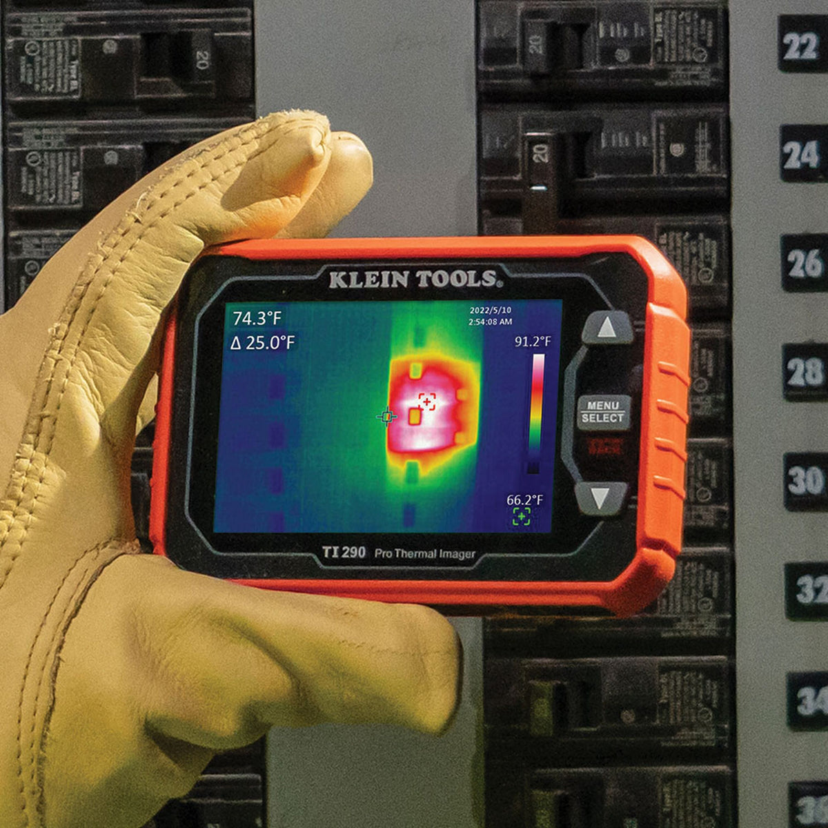 Action shot of a professional wearing leather safety gloves using the TI290 thermal imager to inspect an electrical panel. The high-resolution 76,800-pixel display identifies a localized hot spot on a circuit breaker at 74.3 degrees Fahrenheit, demonstrating the tool's precision in electrical troubleshooting.