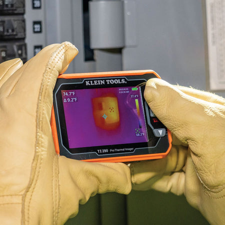 Close-up action shot of a technician using the TI290 Pro Thermal Imager to scan a residential electrical panel. The high-contrast infrared display pinpoint's a localized heat signature on a circuit breaker, demonstrating the tool's effectiveness for professional electrical inspections and predictive maintenance.