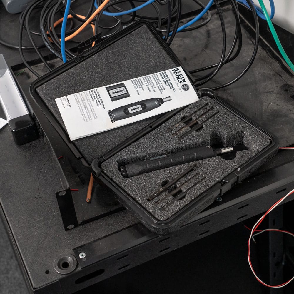 Klein 57032 torque screwdriver set resting inside its foam-cutout hard case with N.I.S.T. calibration manual on an electrical workbench.