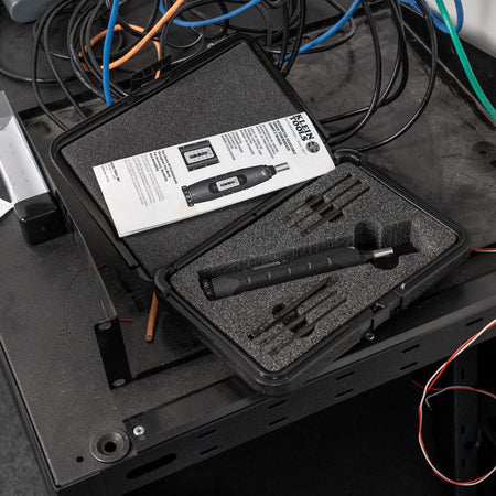 Klein 57032 torque screwdriver set resting inside its foam-cutout hard case with N.I.S.T. calibration manual on an electrical workbench.
