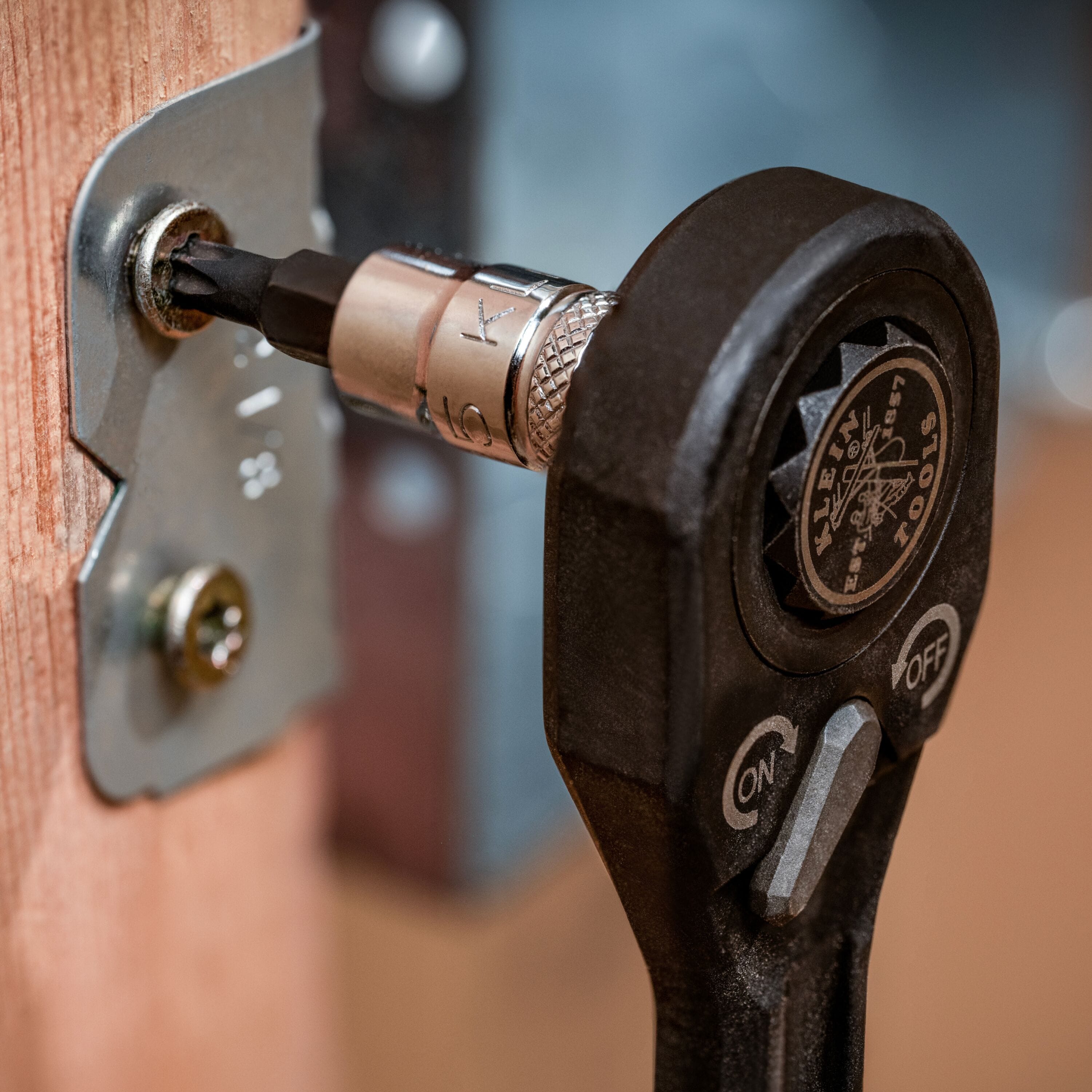 Technician using a ratchet with a Klein TORX bit socket to fasten a structural steel bracket screw on a jobsite wood frame.