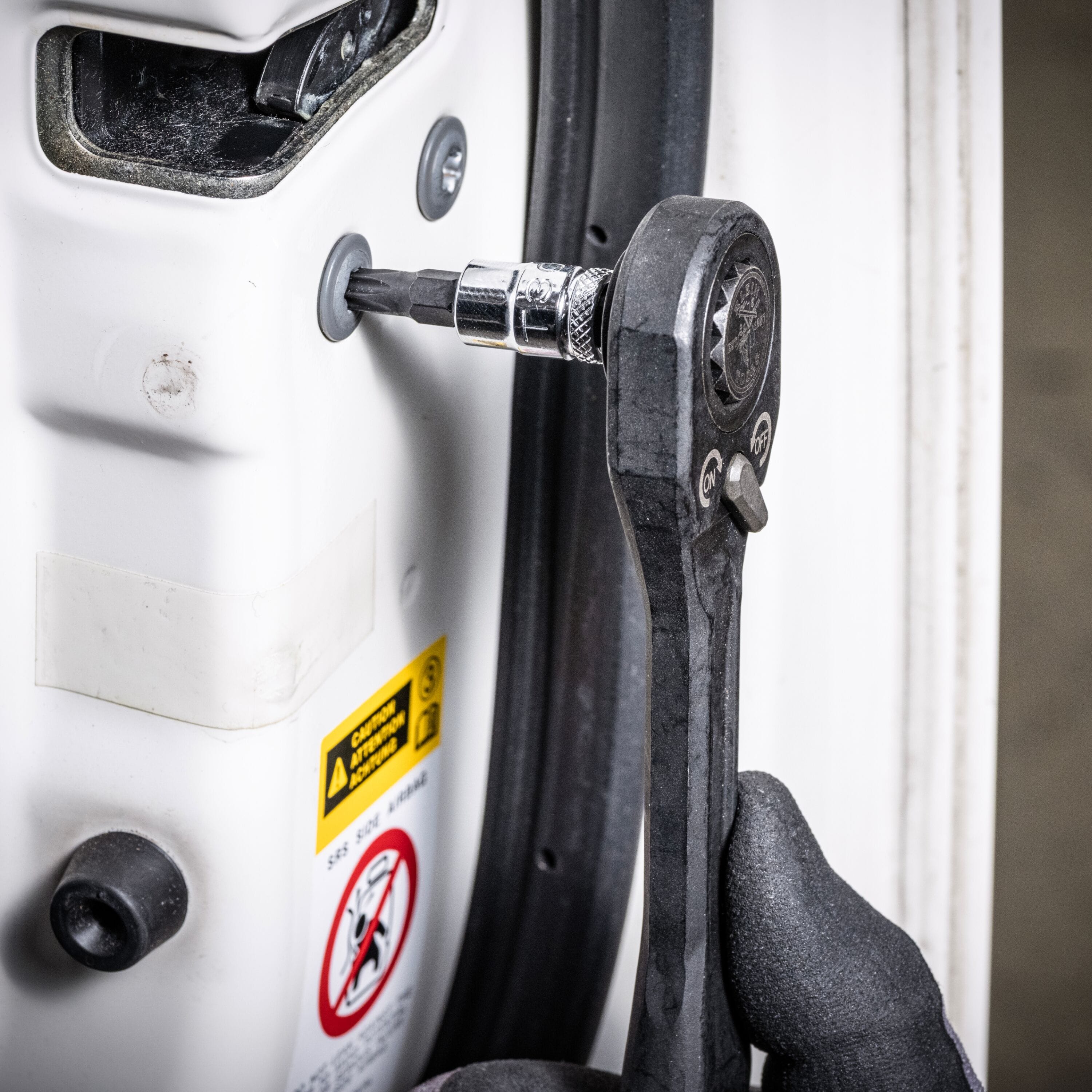 Mechanic using a pass-through ratchet and Klein TORX bit socket to adjust an internal door latch screw on a vehicle frame.