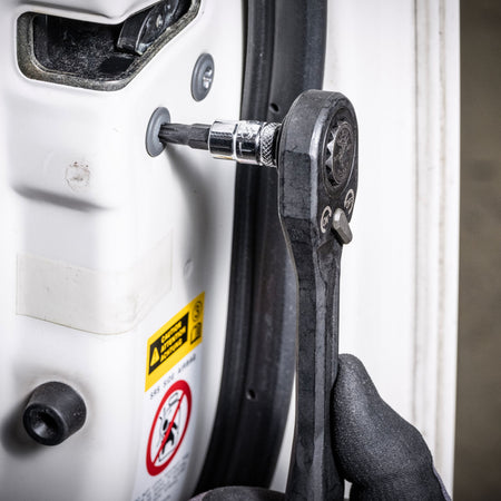 Mechanic using a pass-through ratchet and Klein TORX bit socket to adjust an internal door latch screw on a vehicle frame.