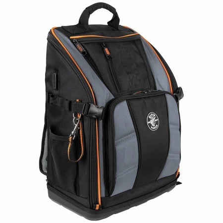 Front three-quarter view of the closed Klein Tools Tradesman Pro Tool Backpack, showcasing its heavy-duty construction, orange accents, and molded base.