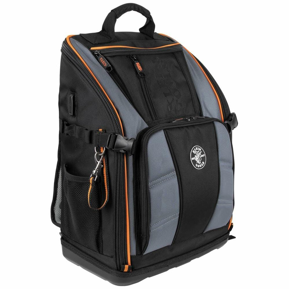 Front three-quarter view of the closed Klein Tools Tradesman Pro Tool Backpack, showcasing its heavy-duty construction, orange accents, and molded base.