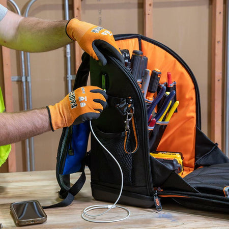 A worker uses the external USB-C port on the backpack to plug in a charging cable for a smartphone, demonstrating the external charging capability.