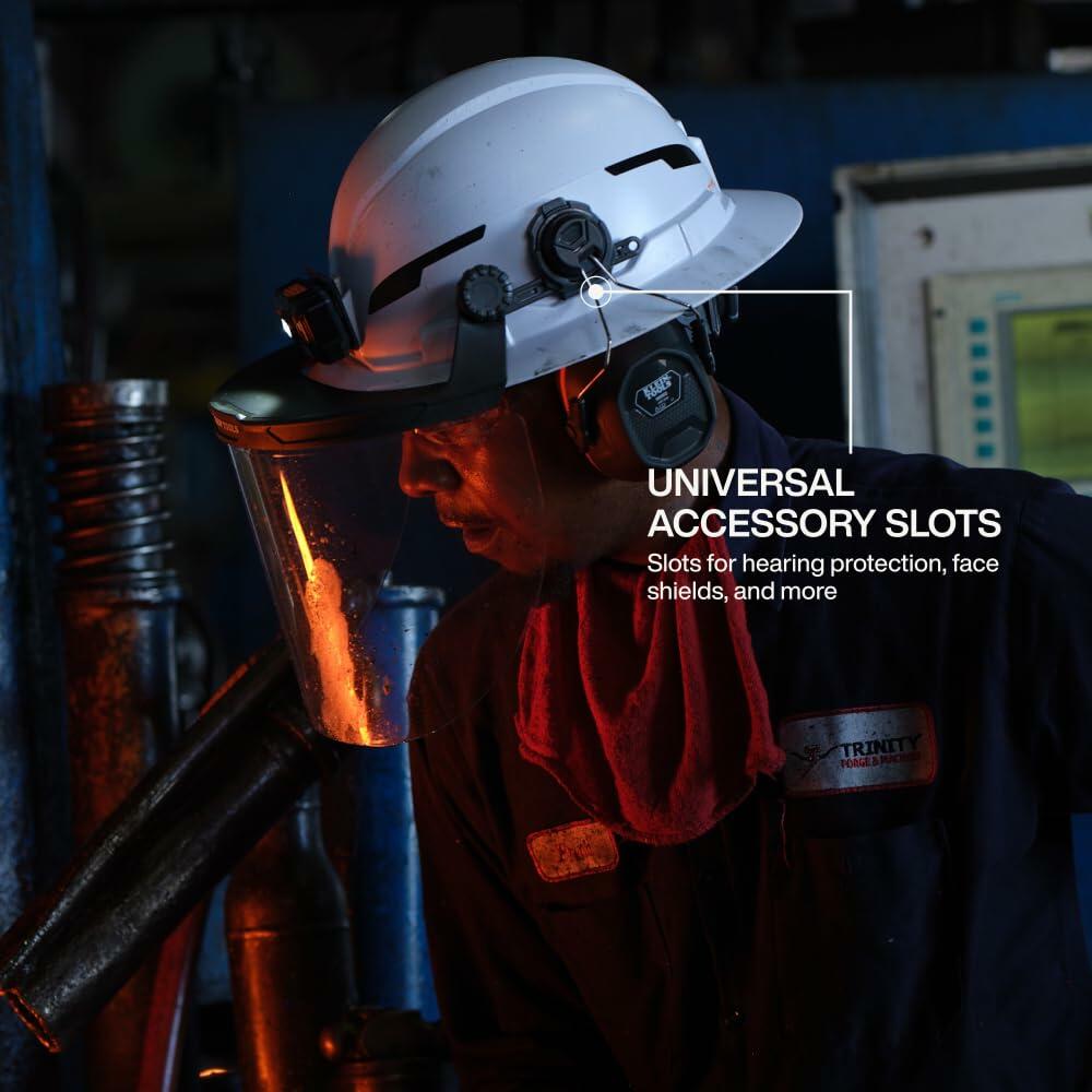 Worker at an industrial forging station wearing the Klein Tools Hard Hat with a face shield and ear muffs attached to the universal accessory slots.