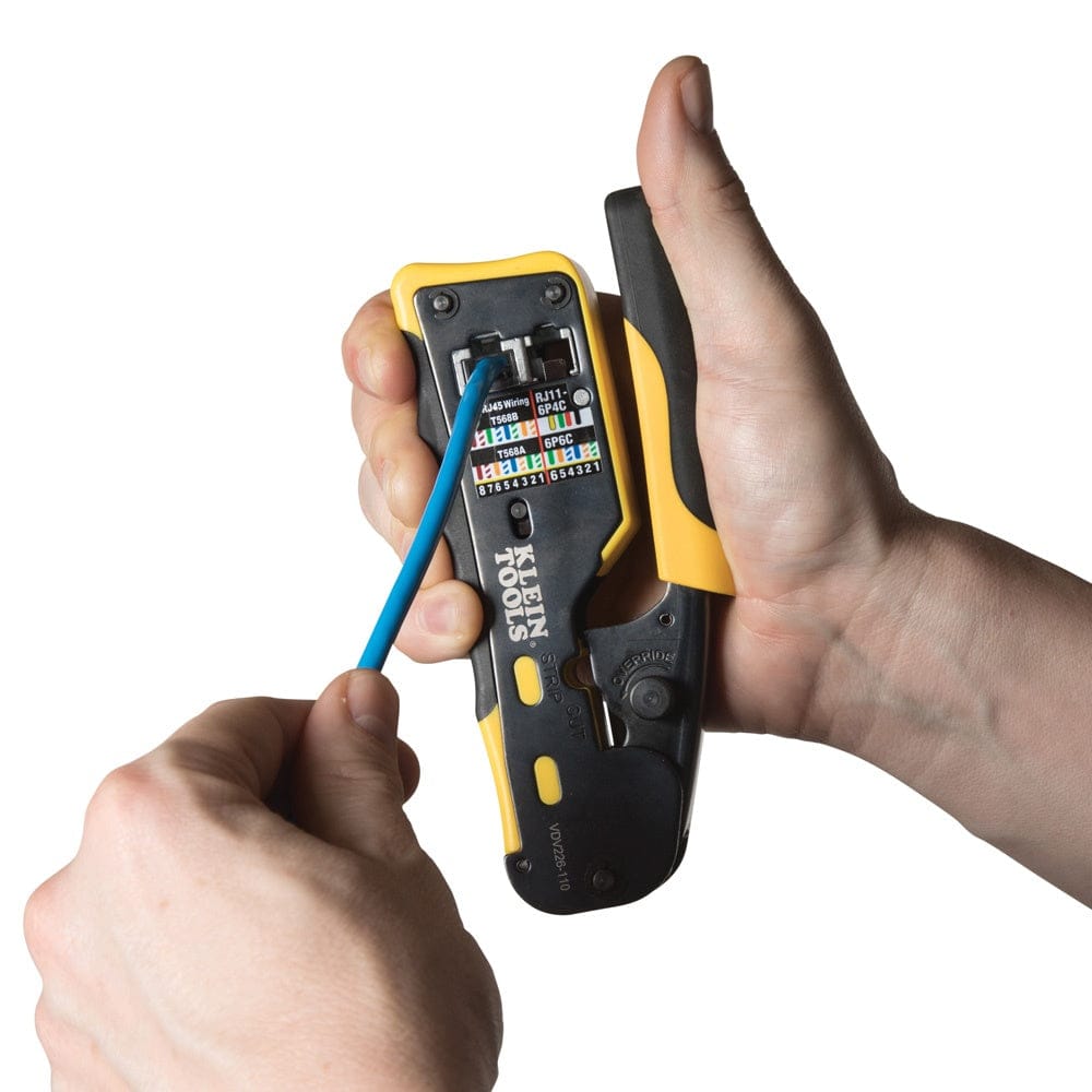 Action shot showing a user's hands using the crimper to terminate a blue ethernet cable, demonstrating the one-handed operation supported by the ergonomic handle design.