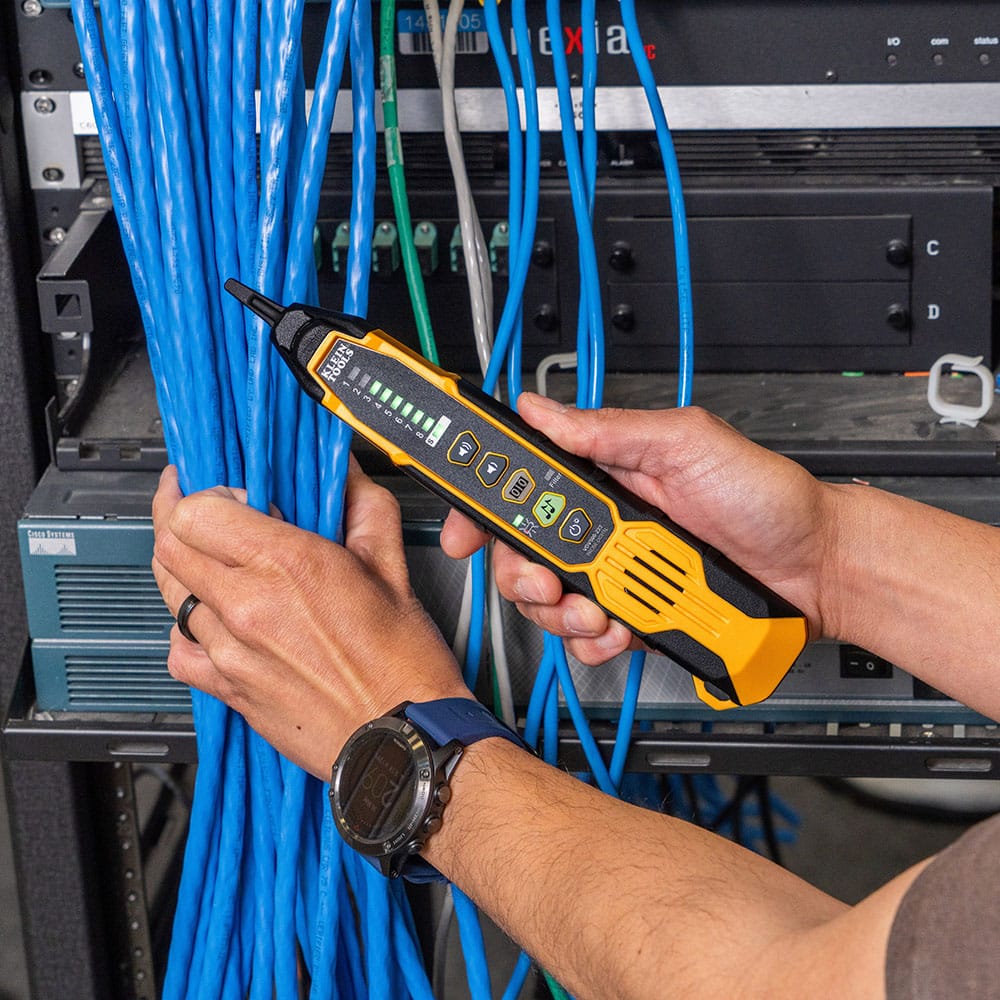 Action shot of a professional identifying cables within a high-density server rack using the VDV500-223 digital tracing probe. The technician is shown scanning a large bundle of blue Ethernet lines, with the probe's signal strength LEDs illuminated to indicate the precise location of the toned pair.