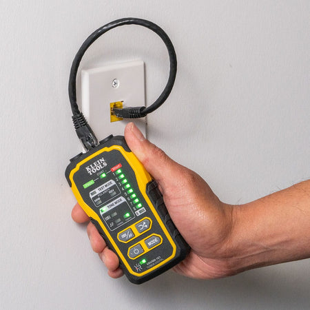 Action shot of a professional technician using the VDV500-163 digital tone generator to verify a network run. The unit is connected to an RJ45 wall plate with a patch cable, showing the diagnostic LED sequence used to confirm continuity, polarity, and pin-to-pin mapping on an active data network.