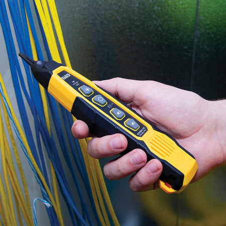 Action shot of a technician using the Klein Tools VDV500123 tracing probe to identify a specific wire within a large industrial electrical panel. The probe's integrated worklight provides clear visibility of the wiring terminals while the responsive tip pinpoint's the correct circuit.