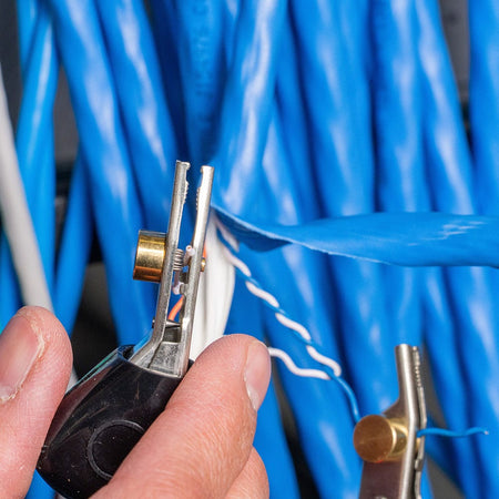 Action shot of a professional using the Klein Tools VDV500163 in an industrial environment. The device is shown providing a digital tone signal through high-quality test leads, illustrating its reliability for troubleshooting complex communication systems on a jobsite.