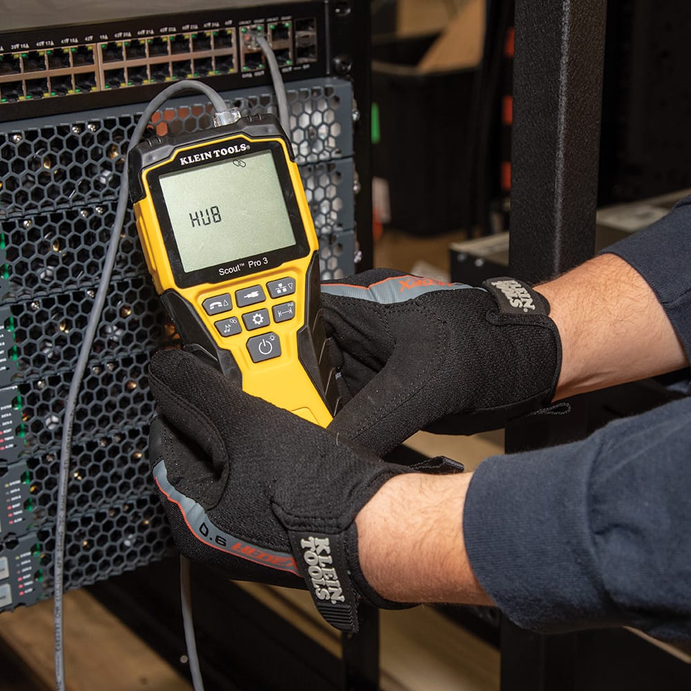 Action shot of a professional technician in a server room using the Scout Pro 3 to identify port locations. The tester is shown in "Hub Blink" mode with the word "HUB" displayed on the backlit screen, allowing the user to visually locate a specific connection on a high-density network switch.