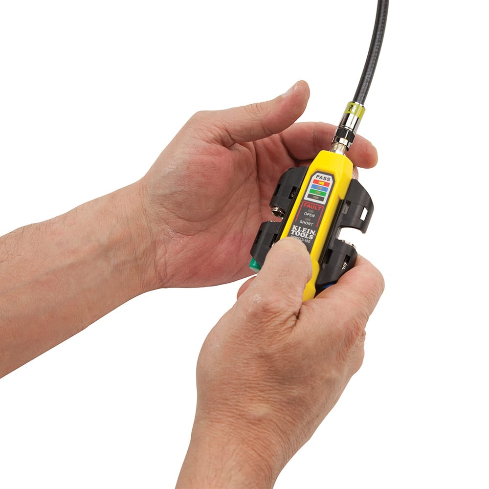 Action shot showing a technician using the VDV512101 to test a coaxial cable. The professional is holding the yellow tester while it is connected to a black coax line, demonstrating the real-time LED feedback used to confirm a successful continuity pass.