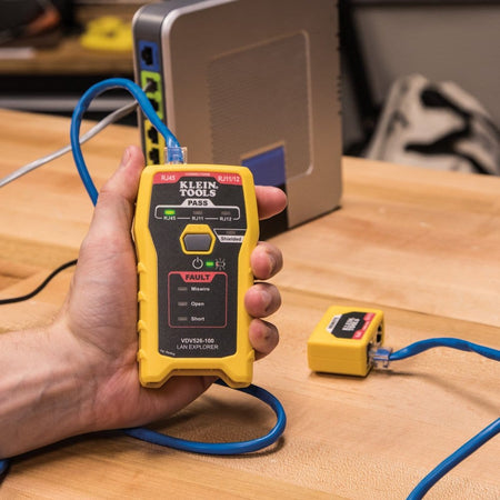 Action shot of a person using the LAN Explorer tester connected to a network device via a blue Ethernet cable, with the green Pass indicator LED illuminated.