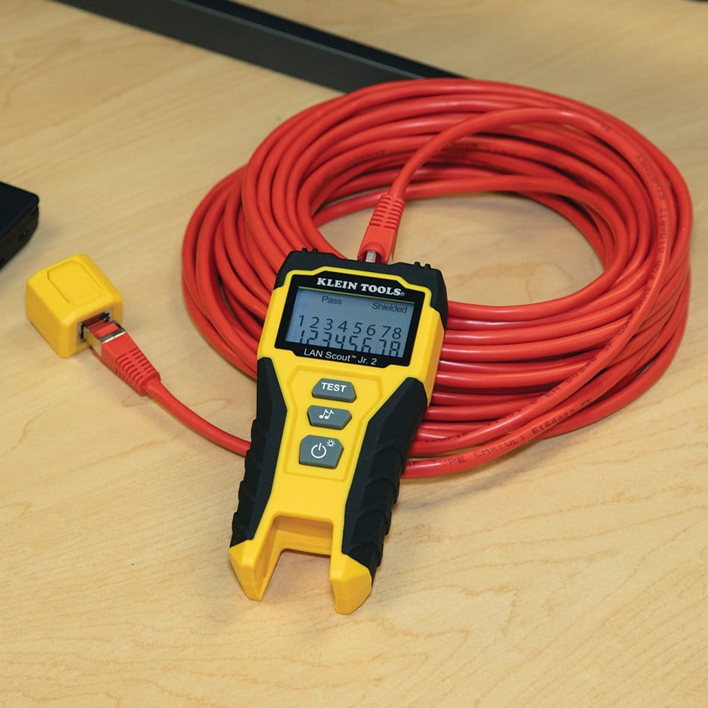 The LAN Scout Jr. 2 tester connected to a large coil of red Ethernet cable, with the display verifying a Pass result and Shielded connection.