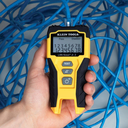Action shot of a person's hands holding the cable tester in a networking environment, verifying a connection amidst a bundle of blue Ethernet cables.