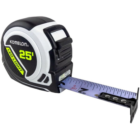 Studio view of the Komelon 25-foot LED tape measure featuring a black and white compact case with the blade slightly extended to show the high-visibility white surface and built-in LED light.