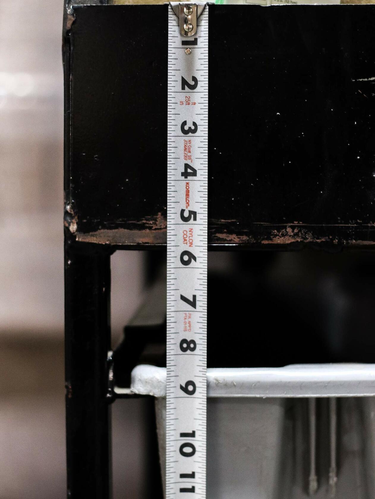 A close-up shot of the Komelon stainless steel measuring tape blade extended and reading an inch measurement on a dark surface, clearly showing the Nylon Coat and Stainless Steel markings.