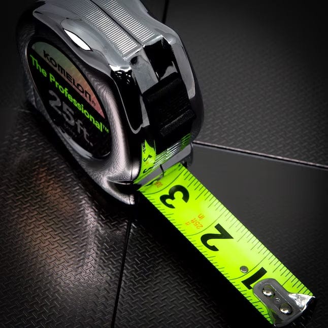 High-contrast studio shot of the Komelon Professional tape measure resting on a dark textured surface, demonstrating the extreme visibility of the neon yellow blade against dark backgrounds.