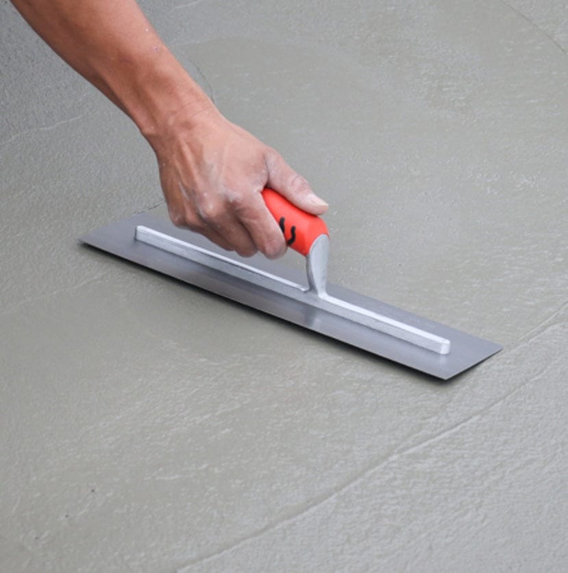 A concrete finisher using the Kraft Tool carbon steel trowel to smooth a wet cement surface holding the ergonomic orange handle.
