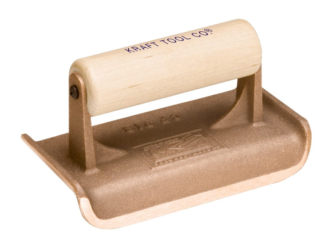 Studio view of the Kraft Tool bronze concrete hand edger featuring a cast bronze body with a curved radius edge and a smooth wood handle stamped with the brand logo.