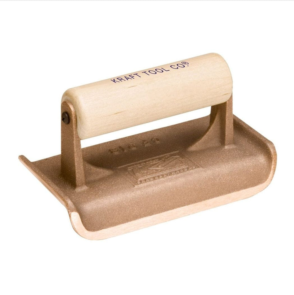 Studio view of the Kraft Tool bronze concrete hand edger featuring a cast bronze body with a curved radius edge and a smooth wood handle stamped with the brand logo.